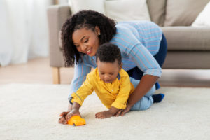 happy african american woman and baby playing with toy car together on carpet